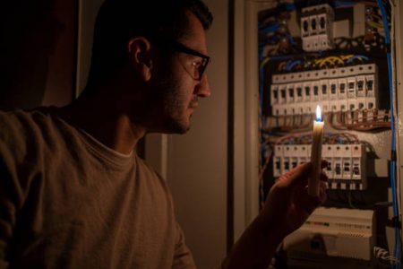 Man Checking Home Fuse Box By Candlelight During Power Outage . Blackout Concept.